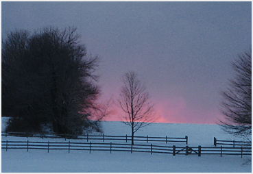 Pink sunlight illuminates snow squalls in the distance.